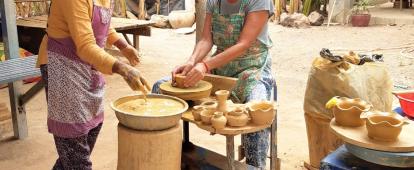 A Cambodian woman teaches a senior volunteer traditional Khmer pottery. An older volunteer participates in a pottery class as part of her Khmer cultural experience in Cambodia.